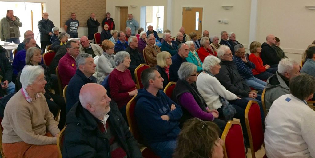 View of packed village hall with people standing at rear